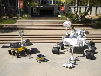 The left vehicle shows the twin Spirit and Opportunity rovers, the center machine is the Sojourner rover, and the car-sized Curiosity is on the right.