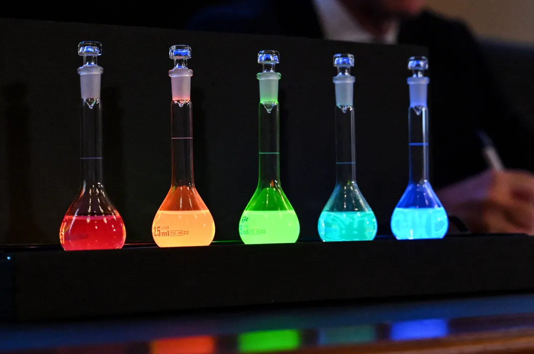 five vials with glowing matter inside. from left to right: red, orange, green, and two shades of blue