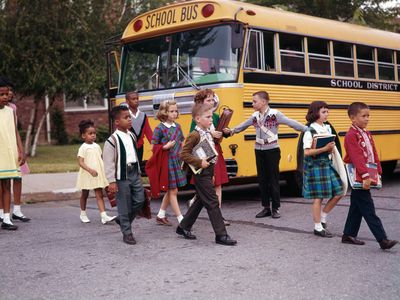 Children cross the street in front of a yellow school bus in 1965.