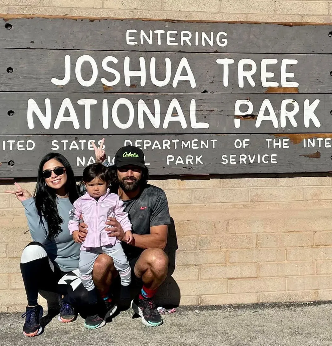 Family with toddler posing in front of national park sign