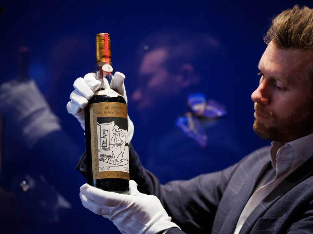 Man wearing white gloves posing with a bottle of whisky